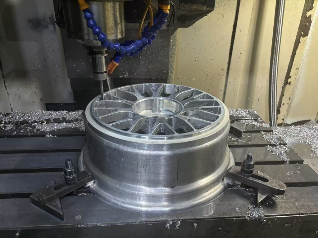 A forged wheel undergoing precision CNC machining, with a milling tool shaping the spokes and outer rim. Metal shavings are visible around the wheel, highlighting the high-precision manufacturing process in an industrial setting.